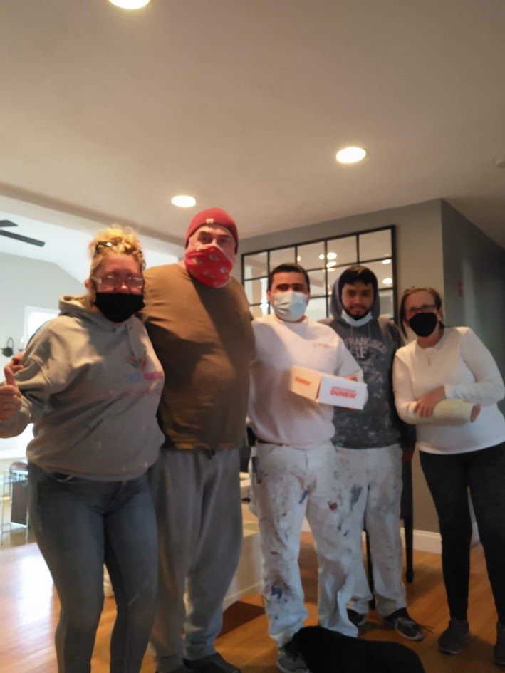 Five masked people stand indoors, posing together and holding papers.