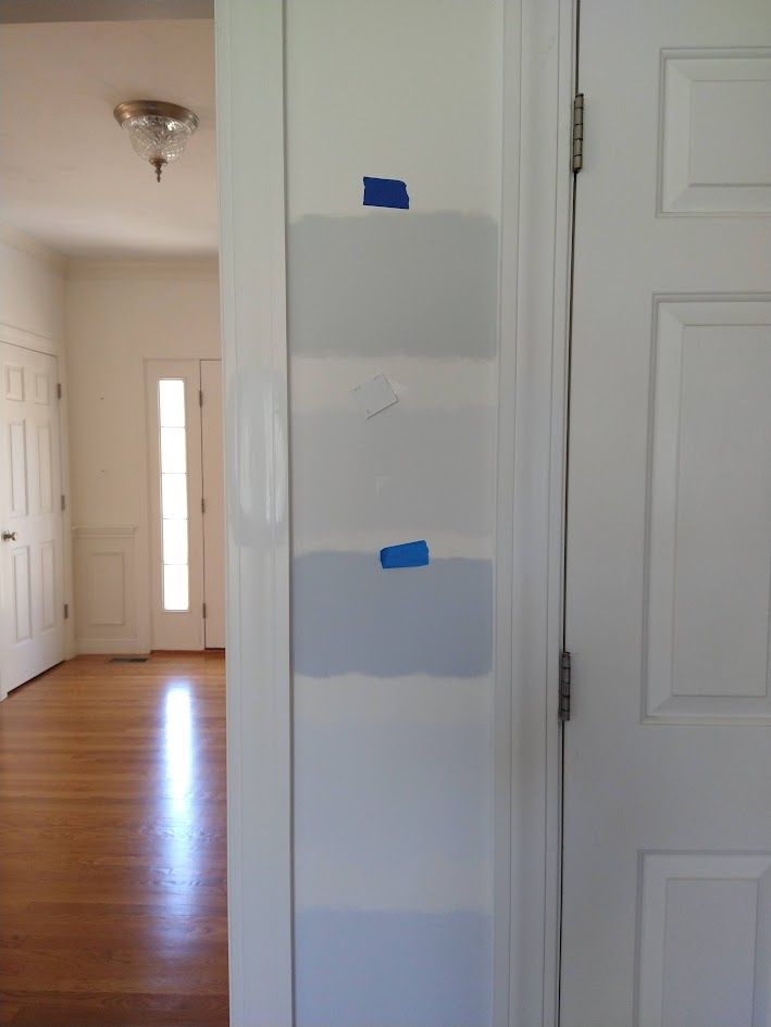 Narrow hallway with a white wall showing several gray paint test patches and blue painter’s tape beside a doorway