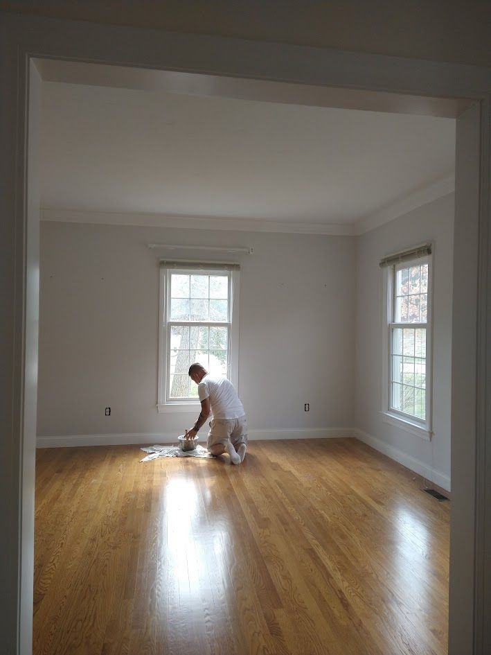 Person mopping a bright empty room with hardwood floors and two windows.