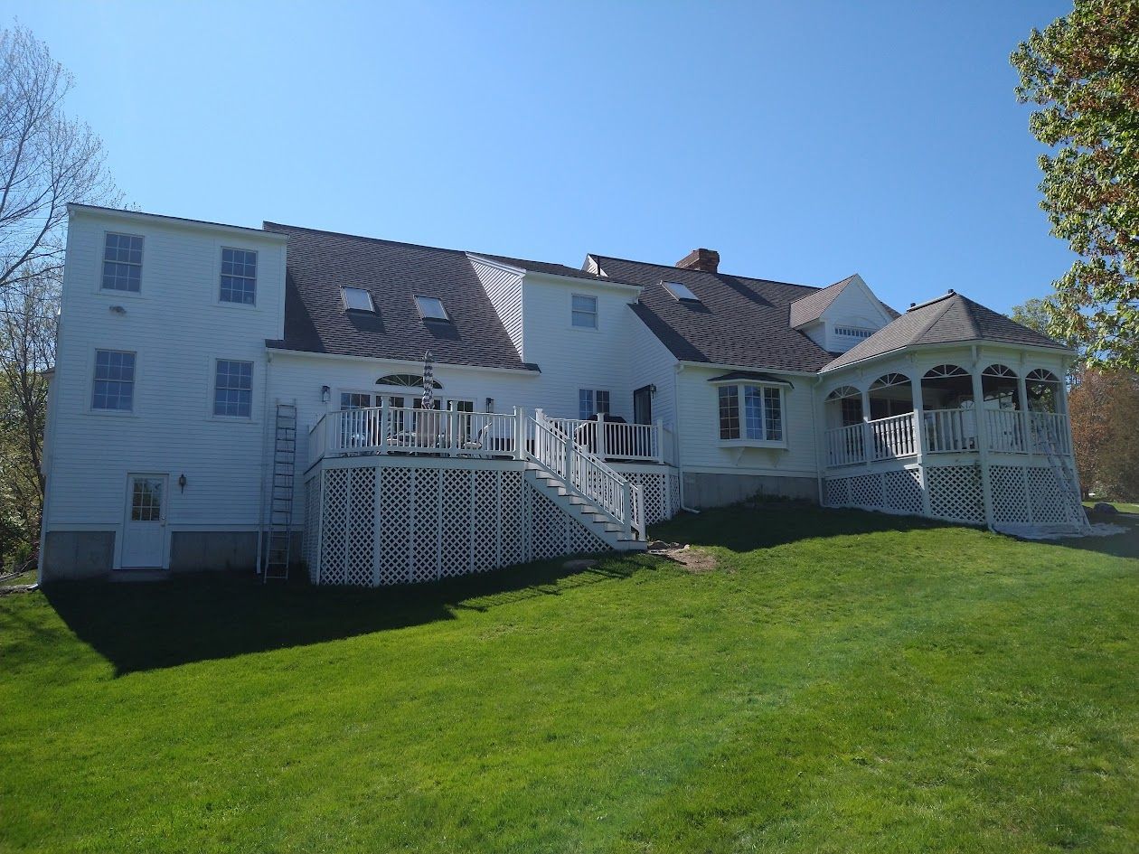 White house with two porches and a green lawn under a clear blue sky