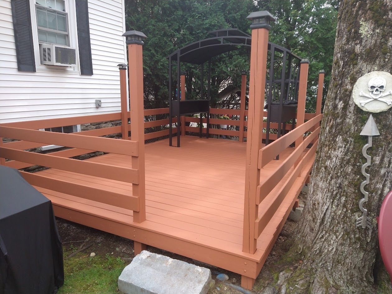 Freshly built wooden deck with orange-brown railings beside a house and yard.