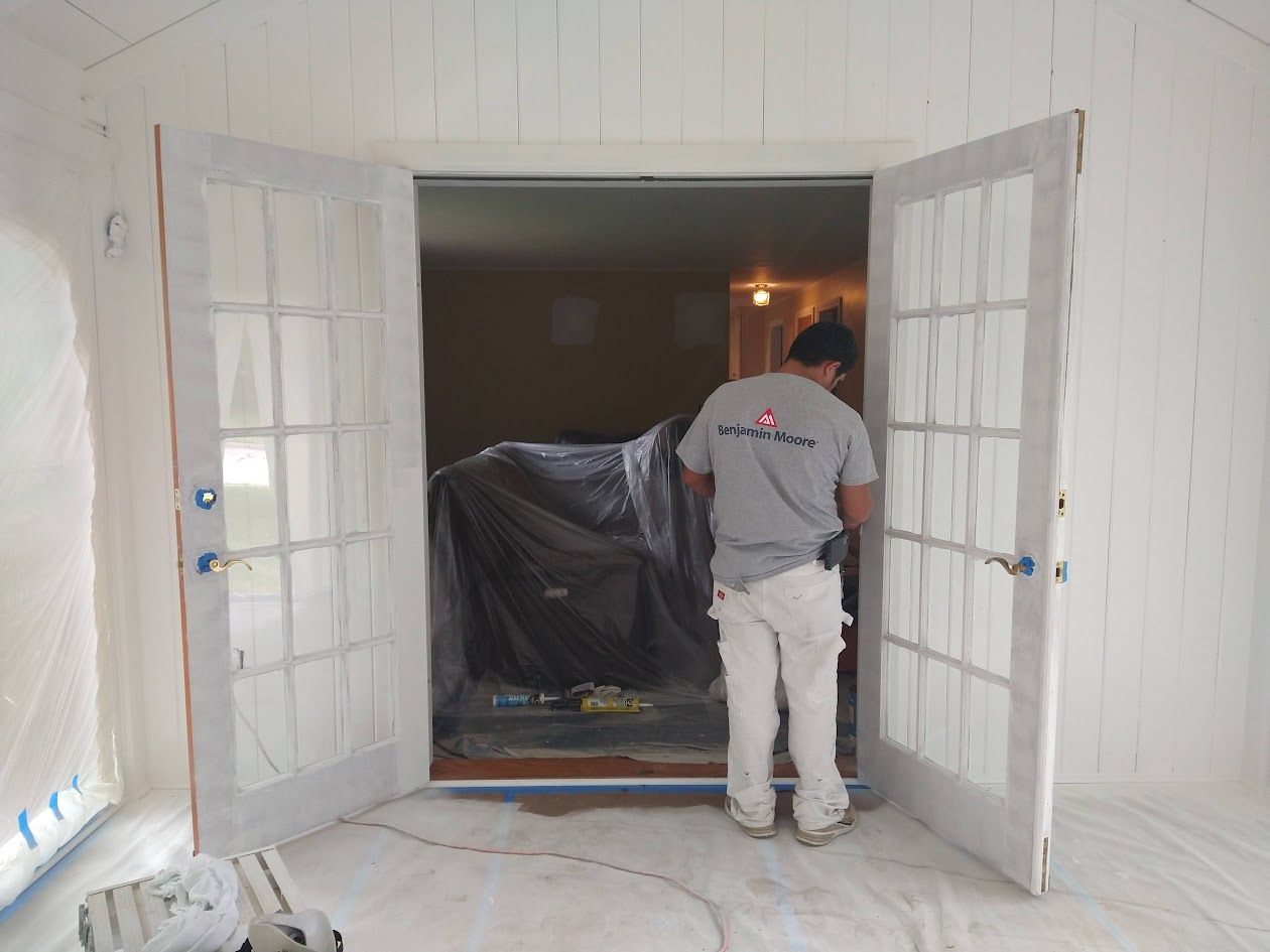 Person standing in a doorway, looking into a dim room with a covered object inside.