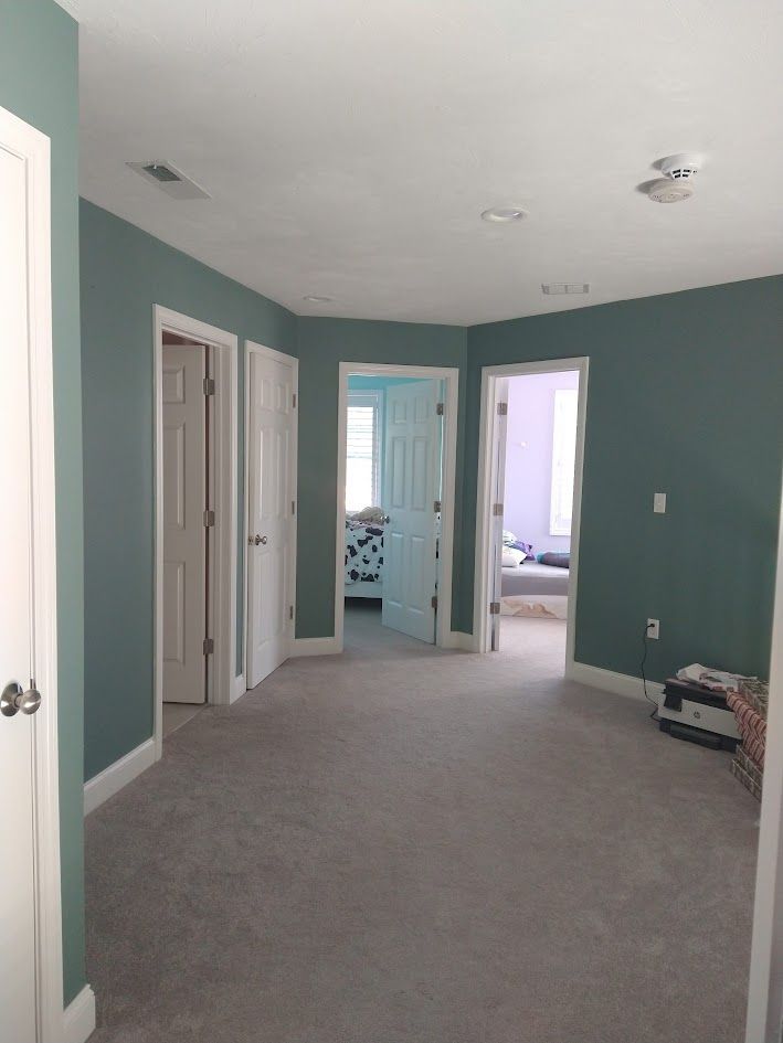 Empty carpeted hallway with teal walls and open doorways in a house