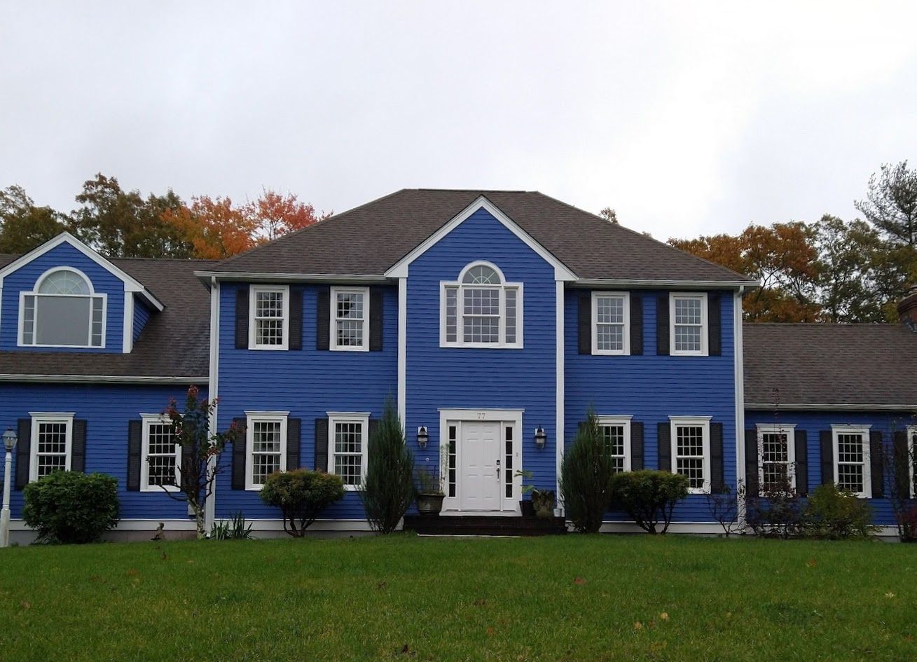 Blue two-story house with white trim and manicured lawn under an overcast sky