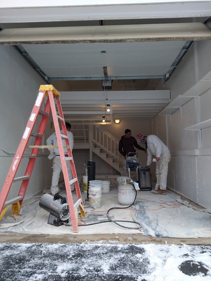 Two workers painting a garage interior, with ladders, buckets, and tools on the floor.