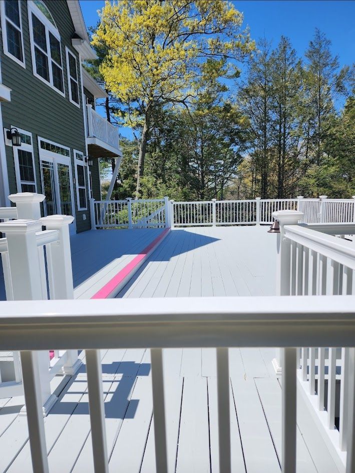 Sunny white deck with white railings beside a green house and trees under a blue sky