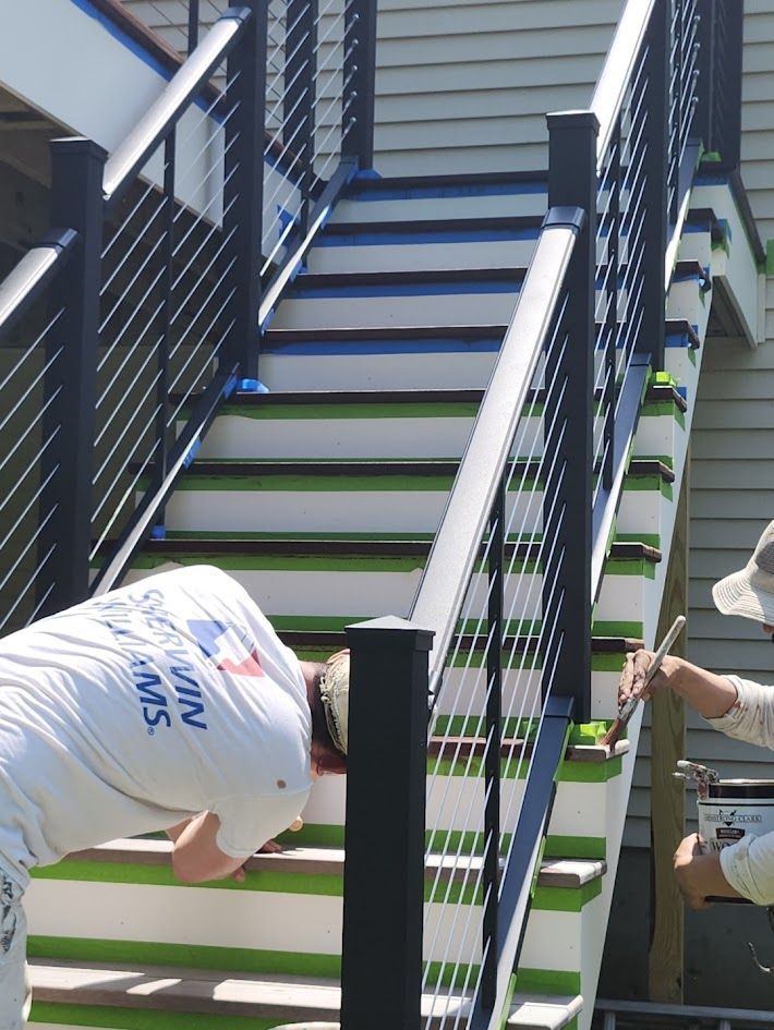 Two workers installing black railings on an outdoor staircase with blue steps and white trim