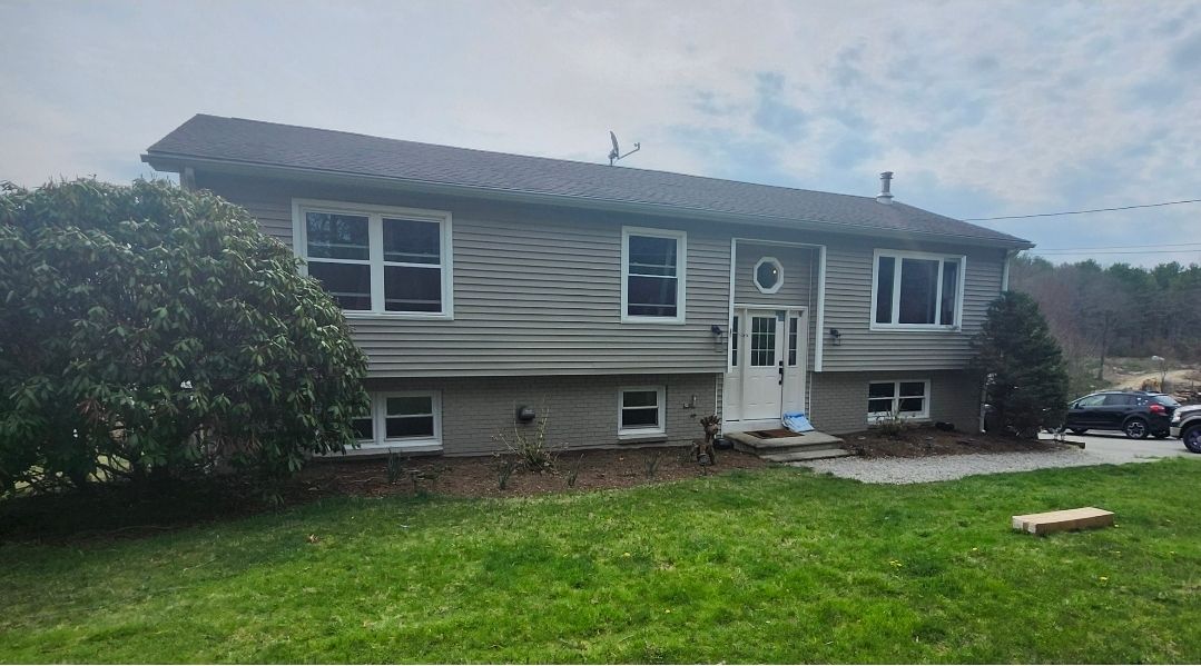 Suburban split-level house with gray siding and a front lawn under a cloudy sky