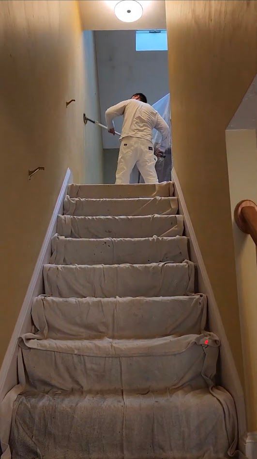 Worker painting a stairwell, with steps covered in protective plastic sheeting.