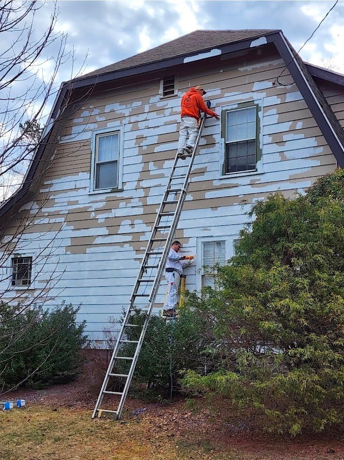 Two workers on ladders repainting a weathered house exterior with peeling white siding.