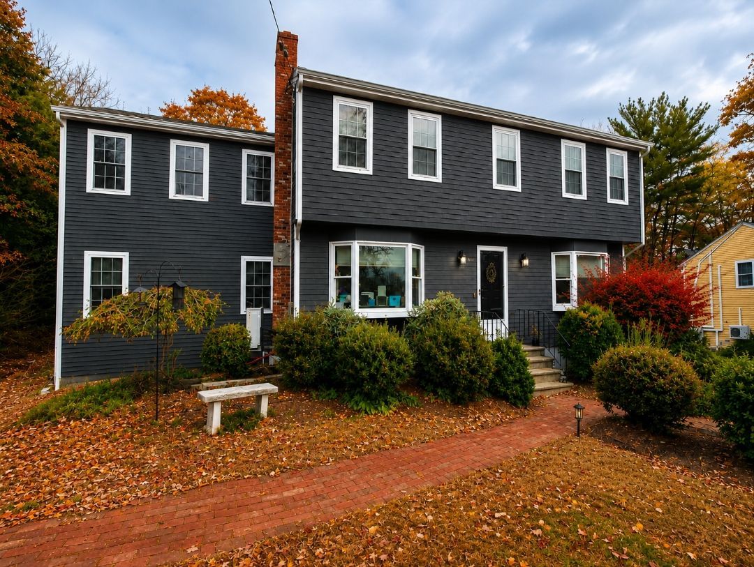Dark gray two-story house with white trim, red brick chimney, and autumn foliage in front yard.
