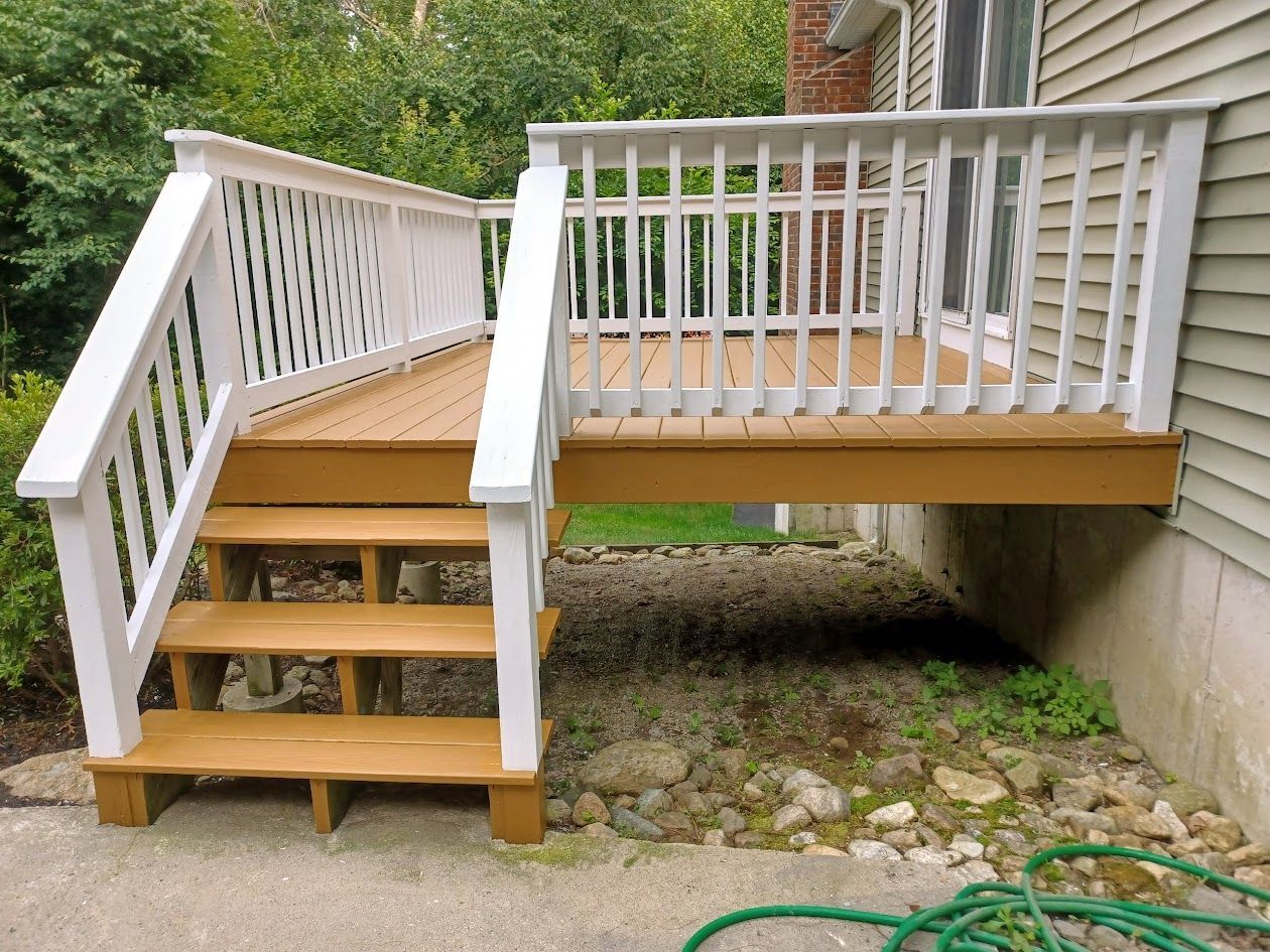 Wooden wheelchair-accessible deck ramp and steps beside a house, with white railings.