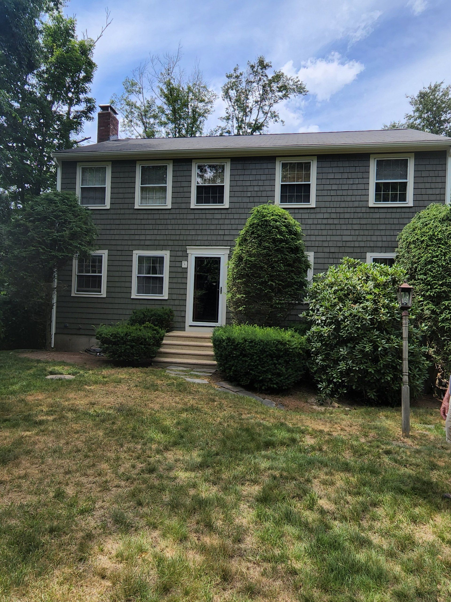 Two-story dark house with a raised deck and white support posts beside a stone retaining wall.