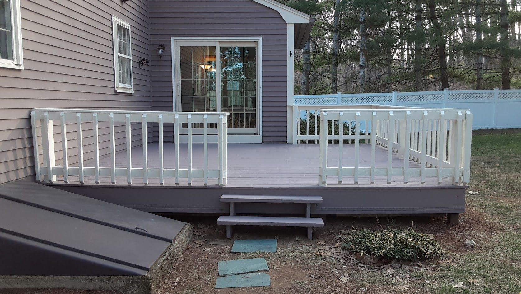 Raised backyard deck with white railings, sliding door, and short central steps leading to a patio.