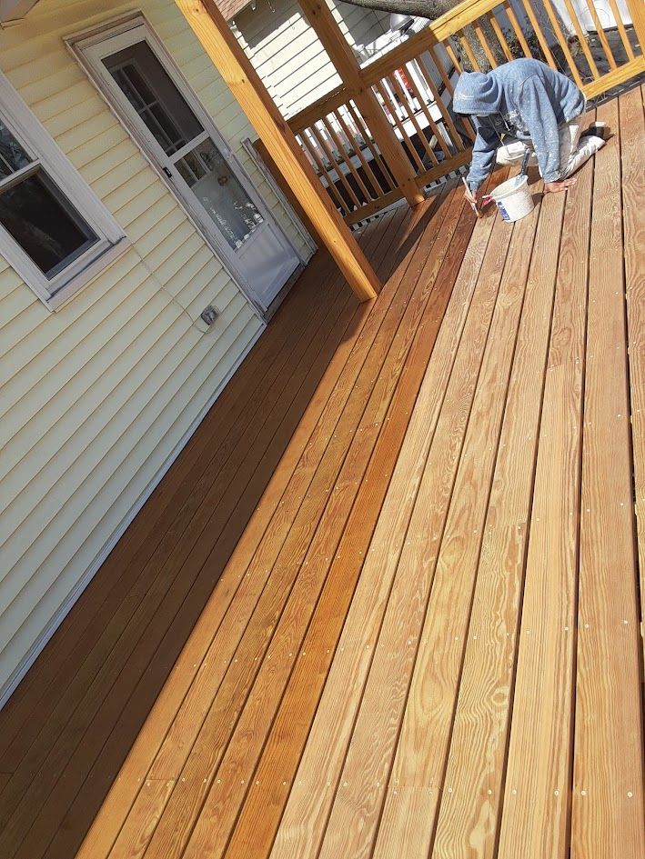 Person kneeling on a wooden deck, working near the railing beside a house.