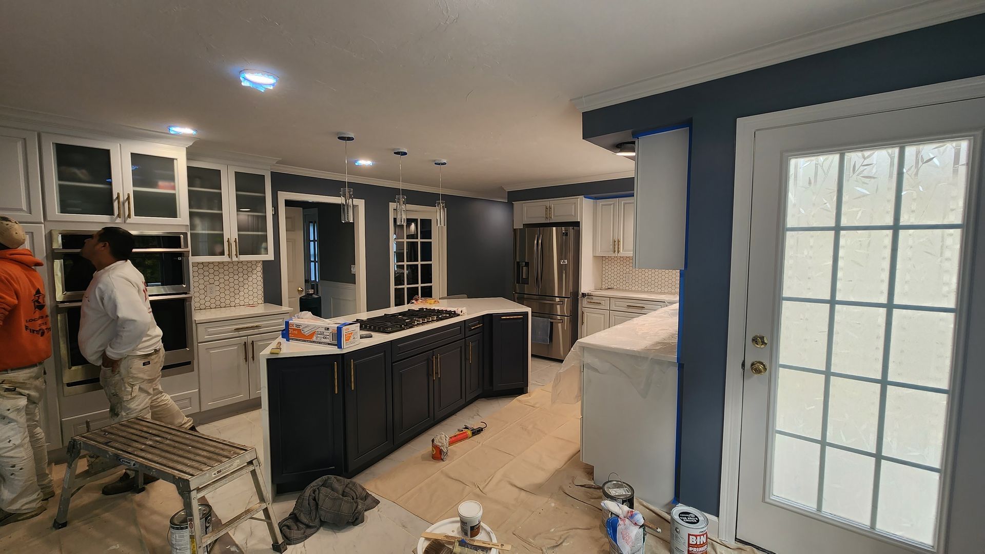 Kitchen under renovation with cabinets, tools, and workers installing countertops