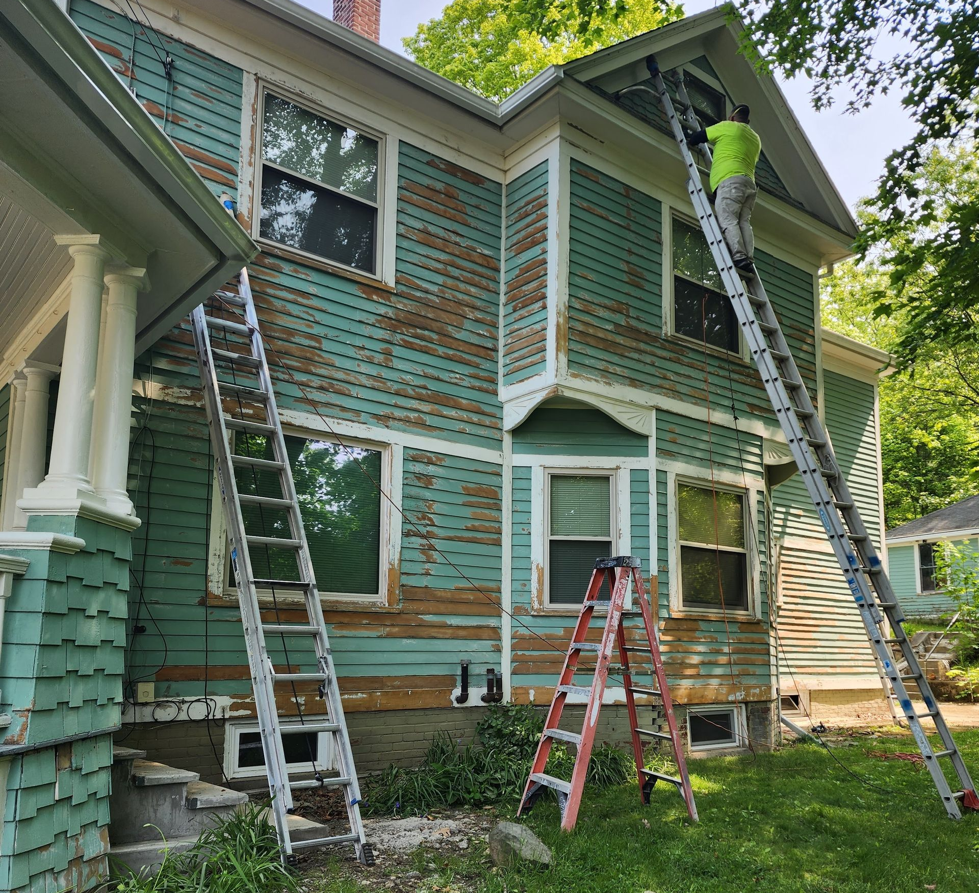 Weathered green house exterior with several ladders leaning against it during repairs