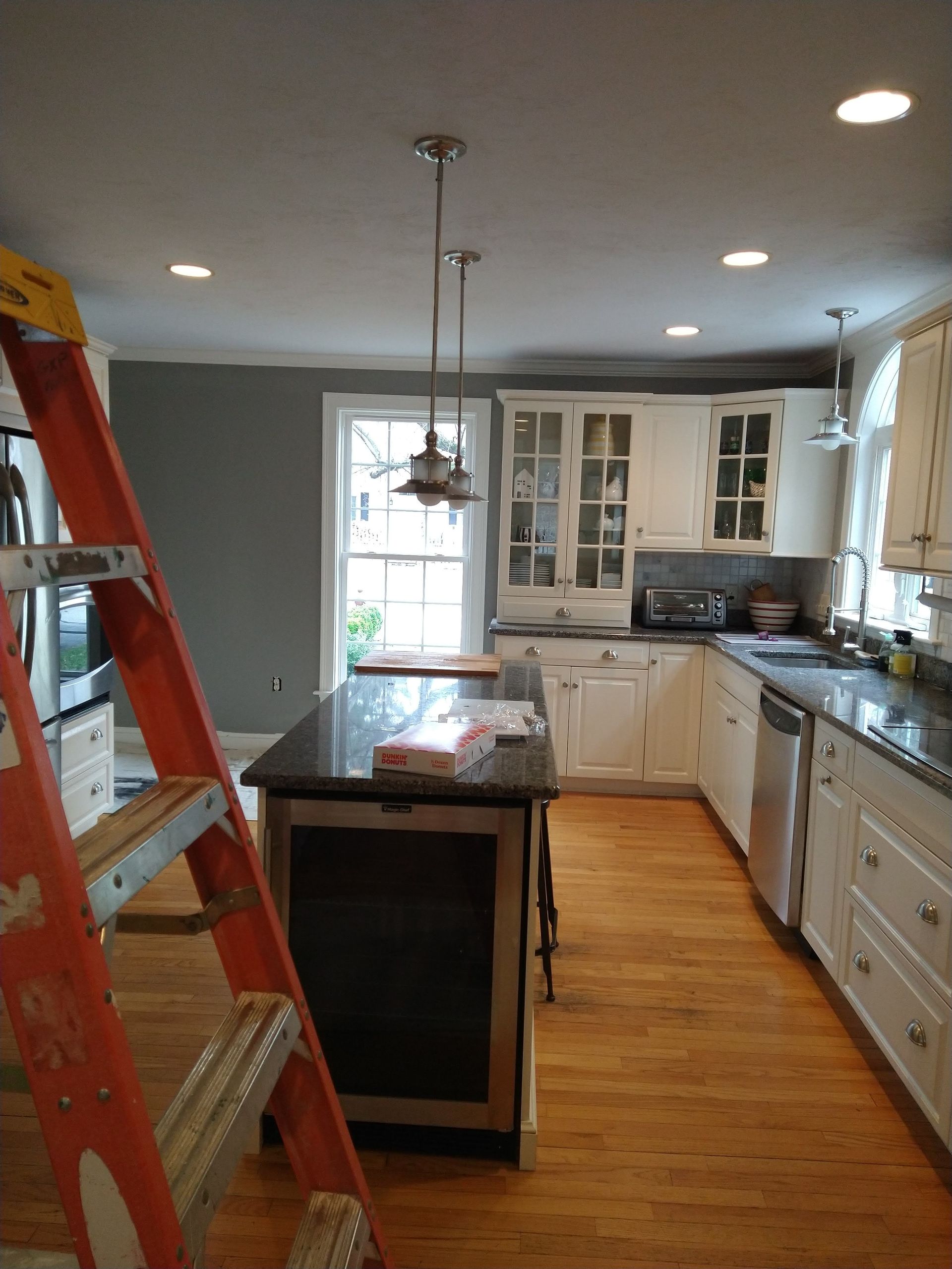 Kitchen renovation with red ladder, dark island, white cabinets, and wood floor