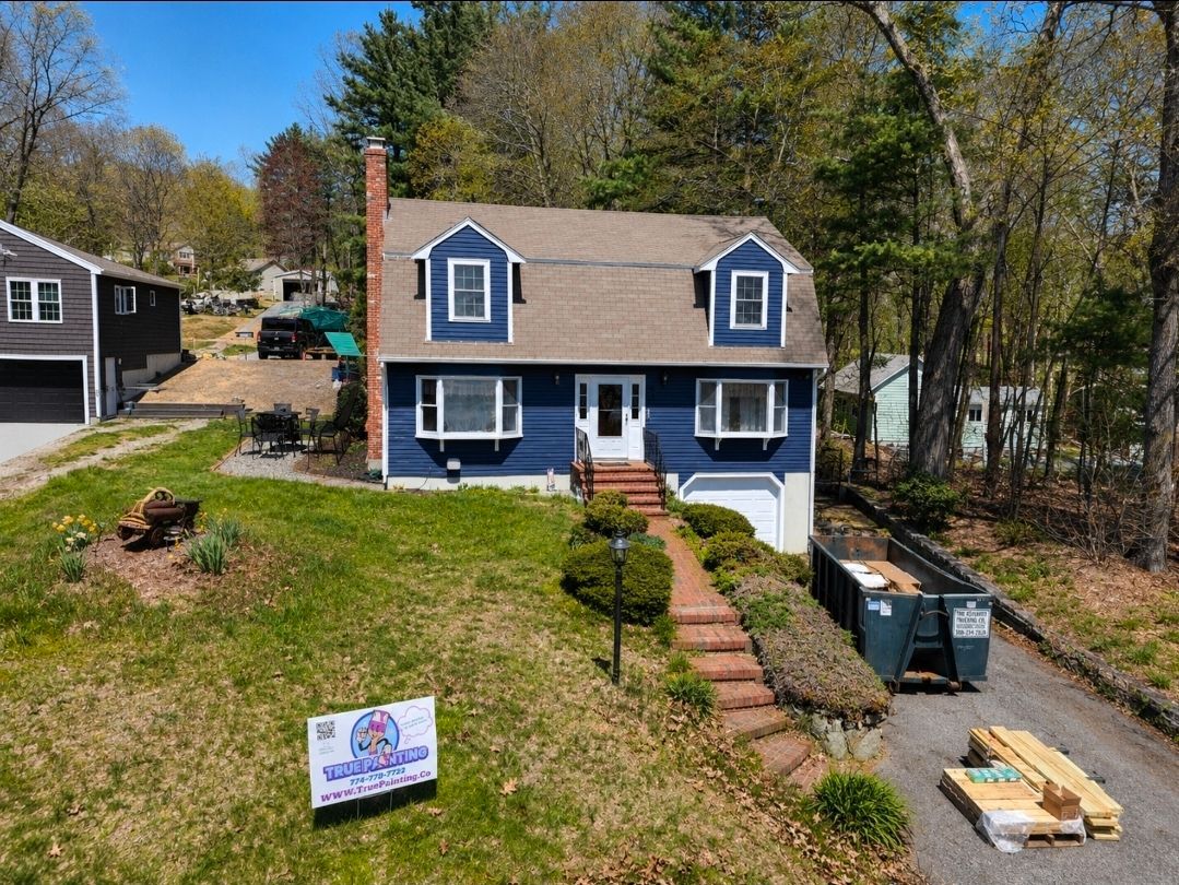 Blue two-story house with white trim, front steps, and a yard with construction materials and a sign
