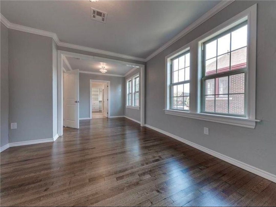Empty modern living room with hardwood floors, gray walls, and large windows letting in natural light