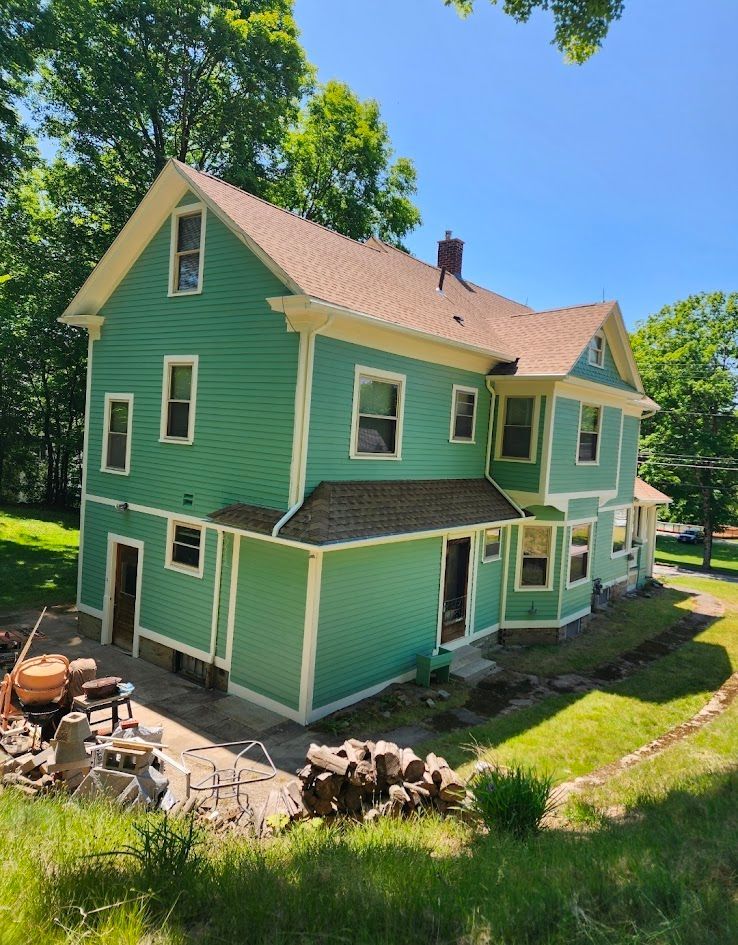 Green two-story house with white trim and a tan roof, viewed from the yard on a sunny day