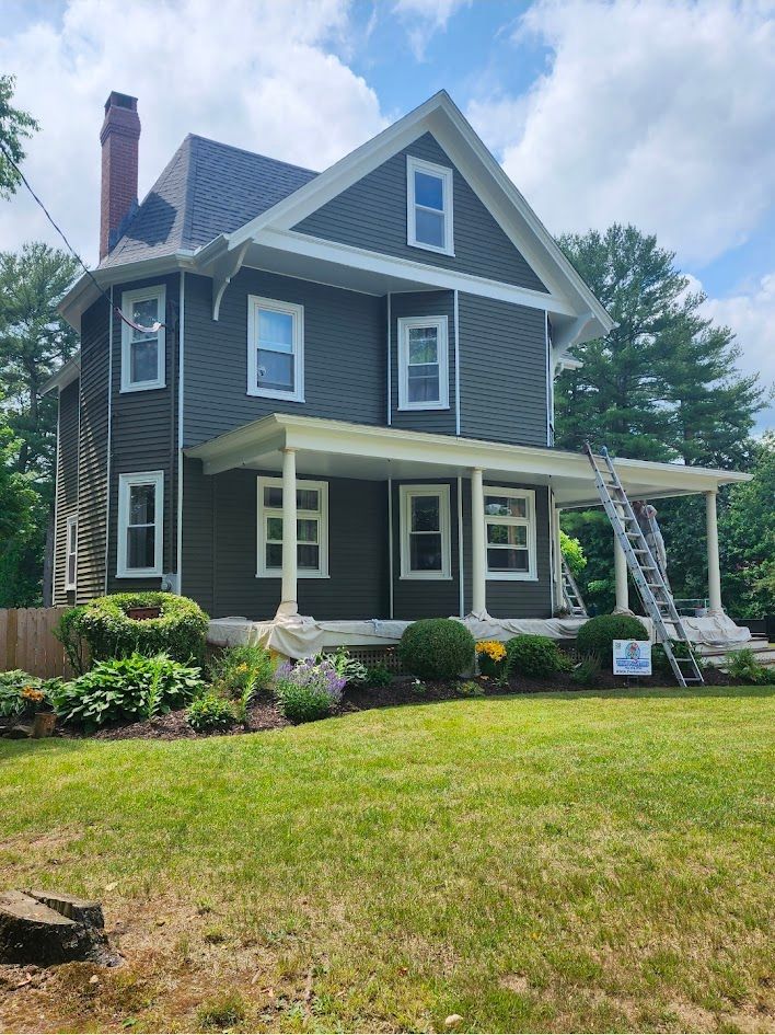 Gray two-story house with white trim, front porch, and well-kept lawn under a blue sky