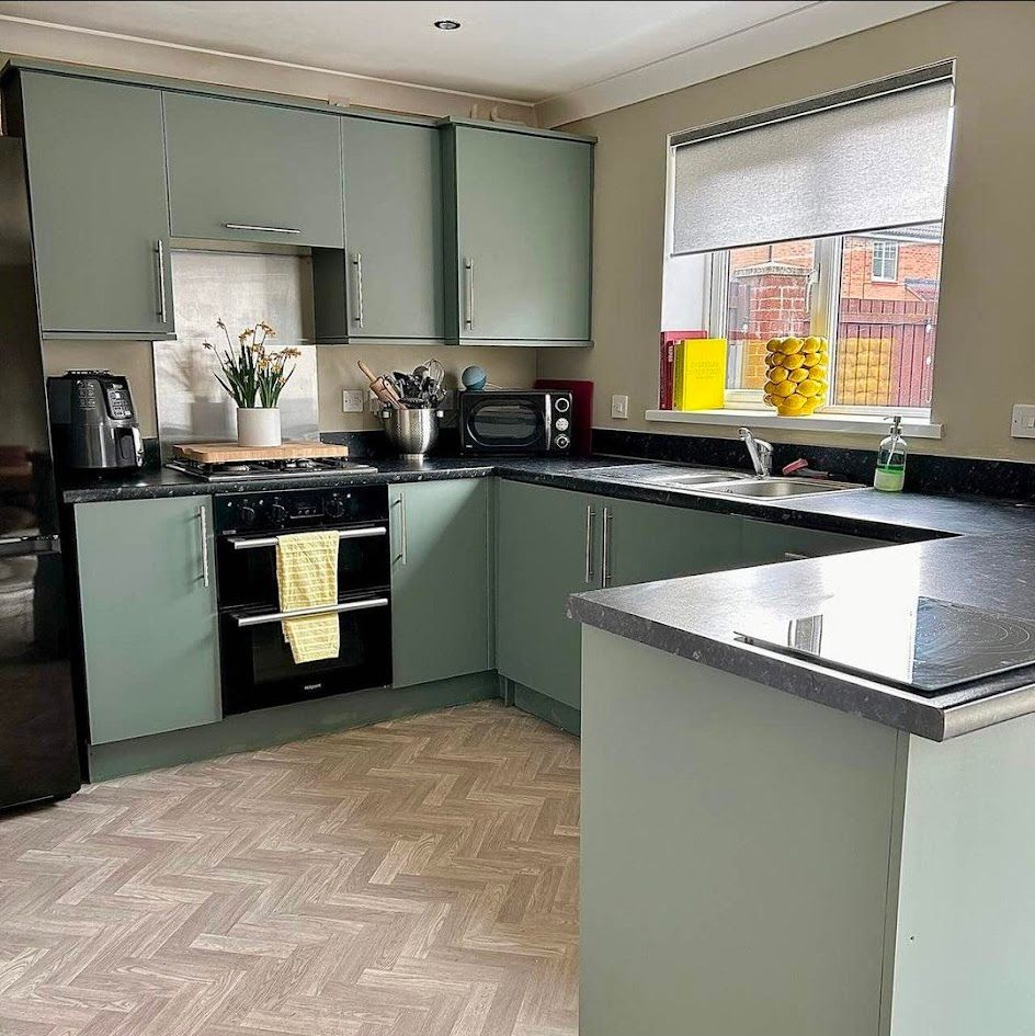 Modern kitchen with sage green cabinets, black appliances, and a window over the sink