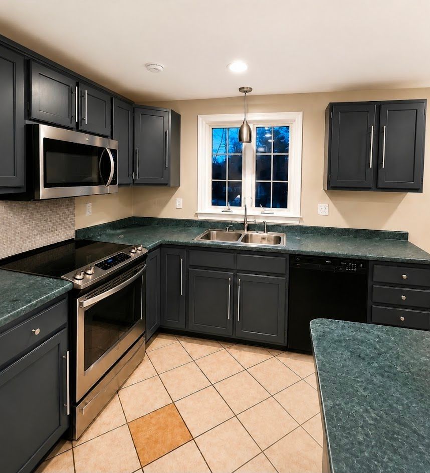 Modern kitchen with dark cabinets, green countertops, stainless appliances, and a window over the sink.