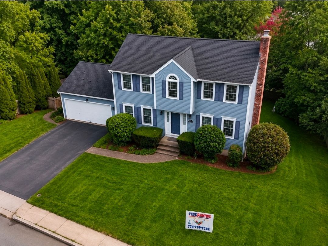 Blue two-story house with white trim, driveway, green lawn, and a for-sale sign
