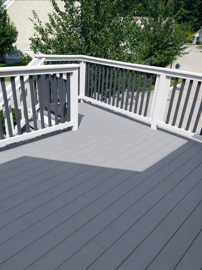 Gray deck with white railings overlooking a tree-filled yard and driveway
