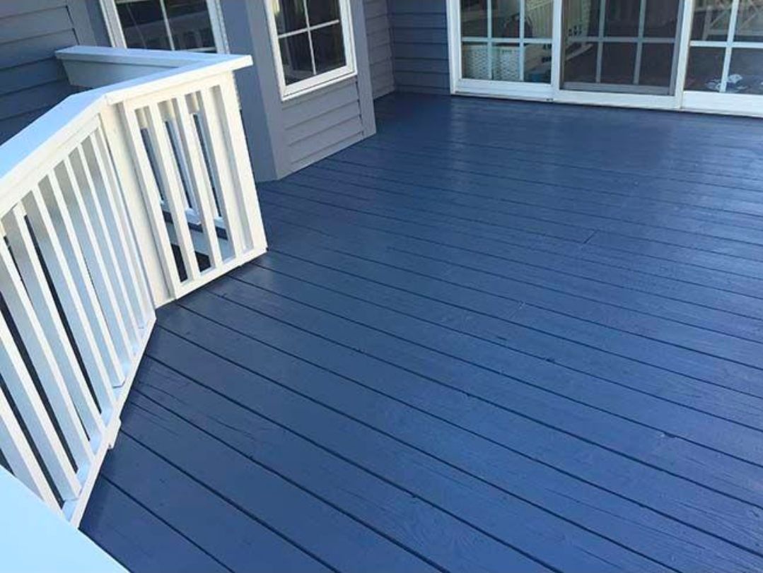 Blue-painted wooden deck with white railing beside a house and sliding glass door