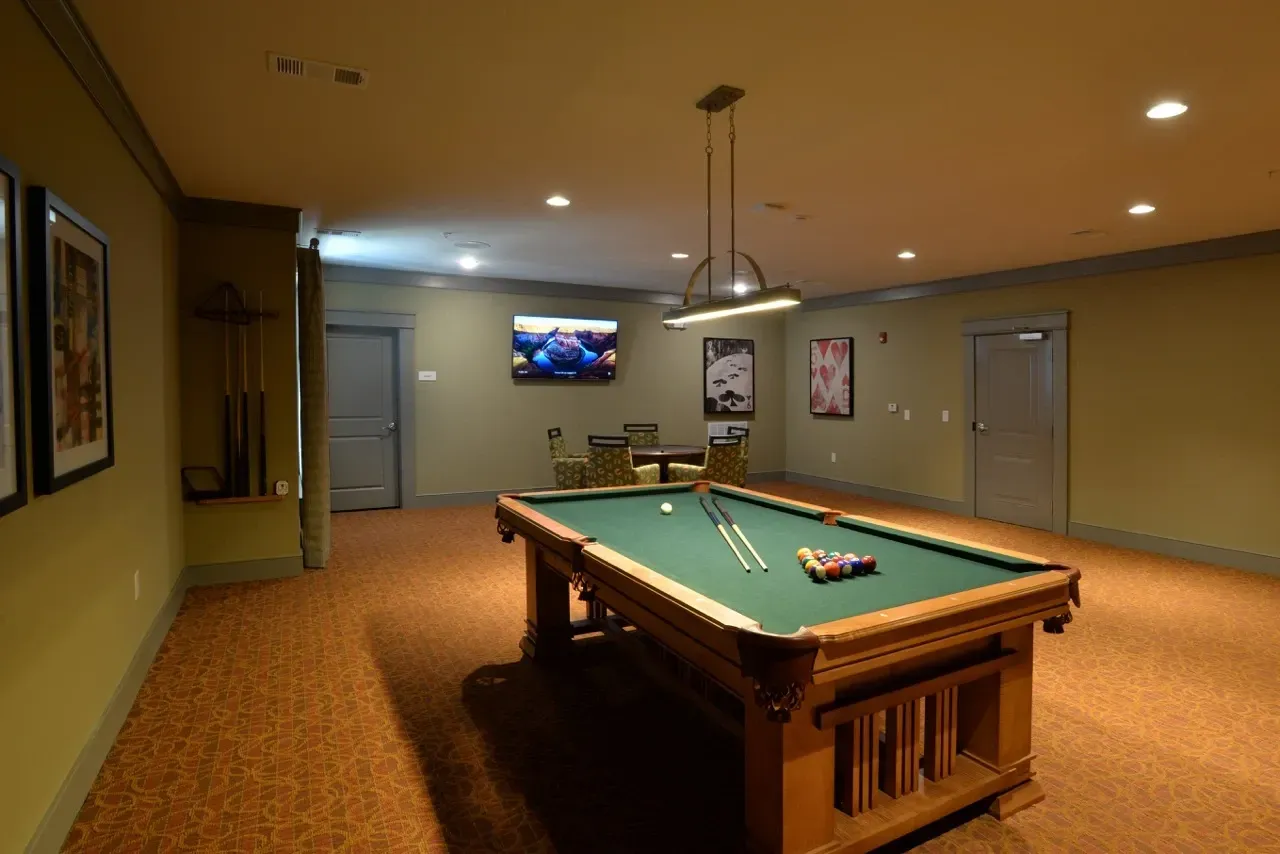 Indoor community recreation room with a pool table, cues, chairs, and wall art.