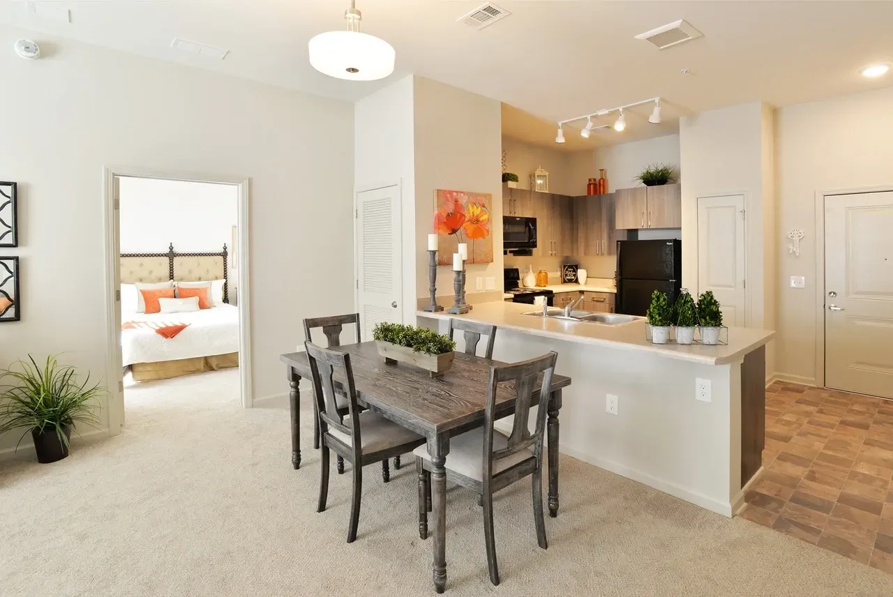 Open-concept dining area with a wood table and kitchen island; bedroom visible through doorway.
