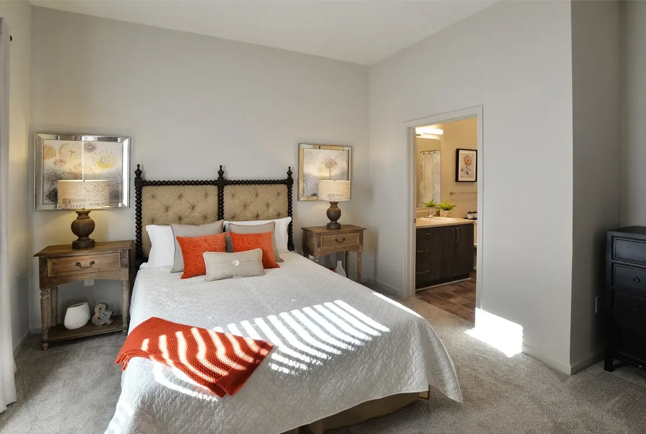 Bedroom in an apartment with a tufted headboard, two nightstands, and a doorway to the bathroom.