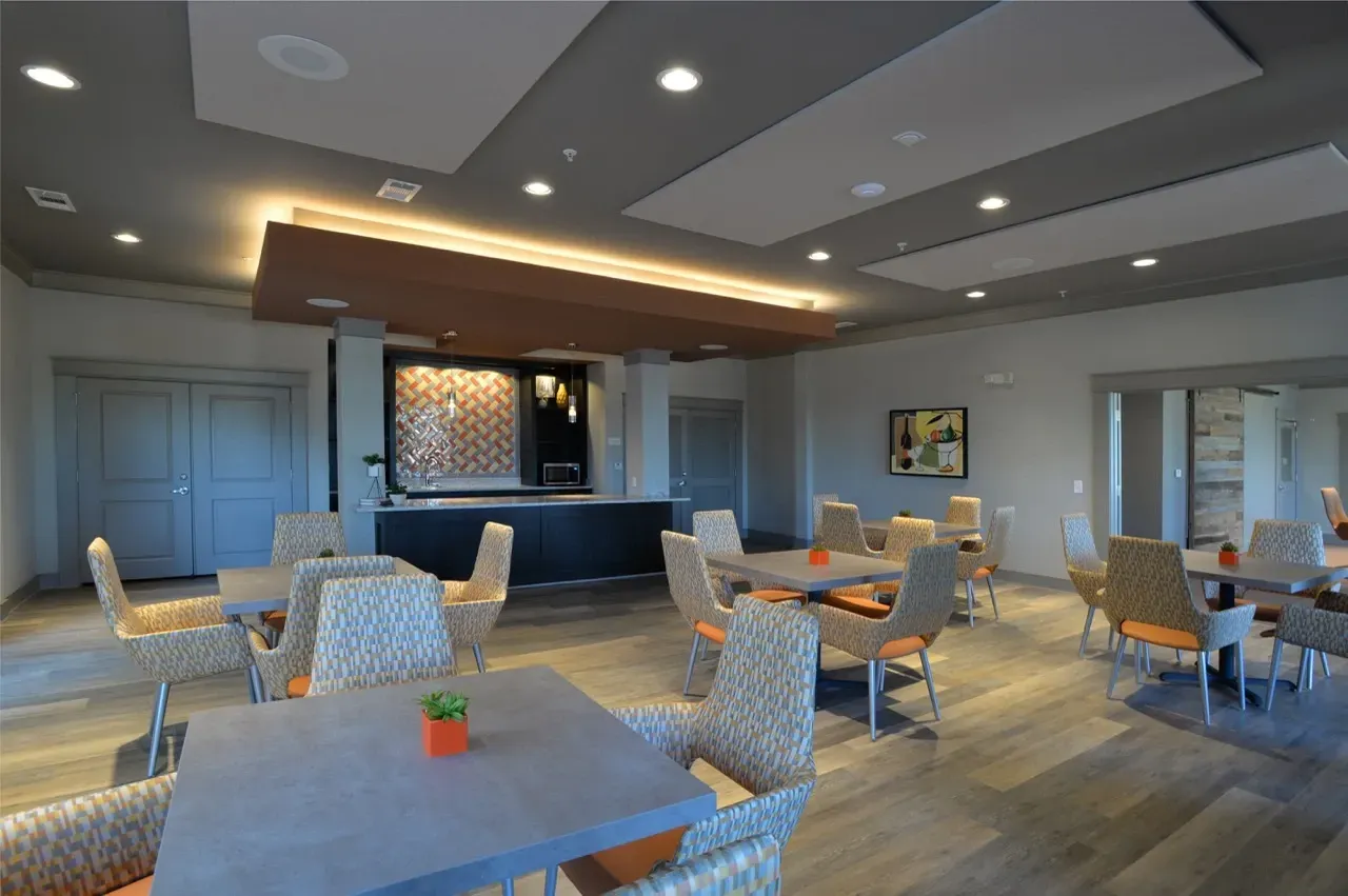 Interior view of a modern resident lounge with seating, tables, and a bar area.