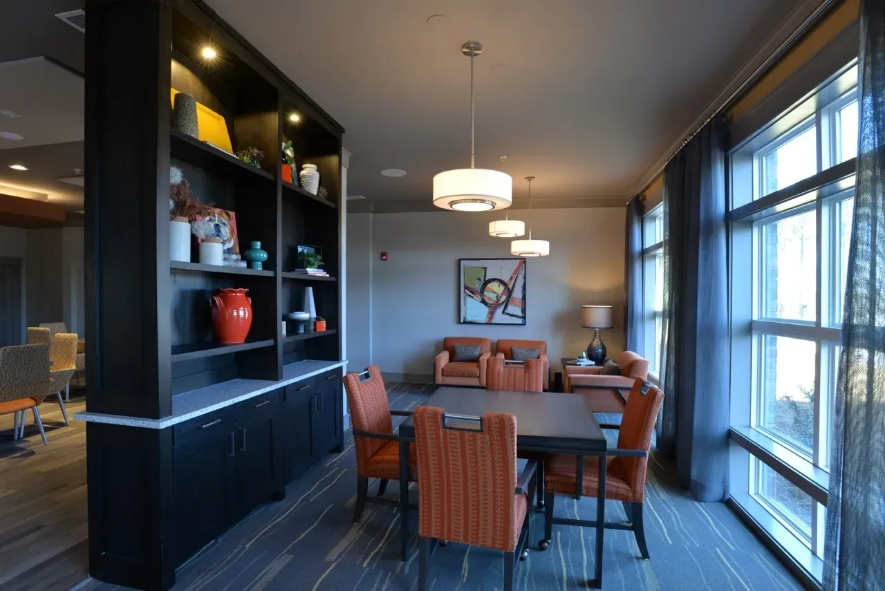 Communal lounge with orange chairs around a table and large windows.
