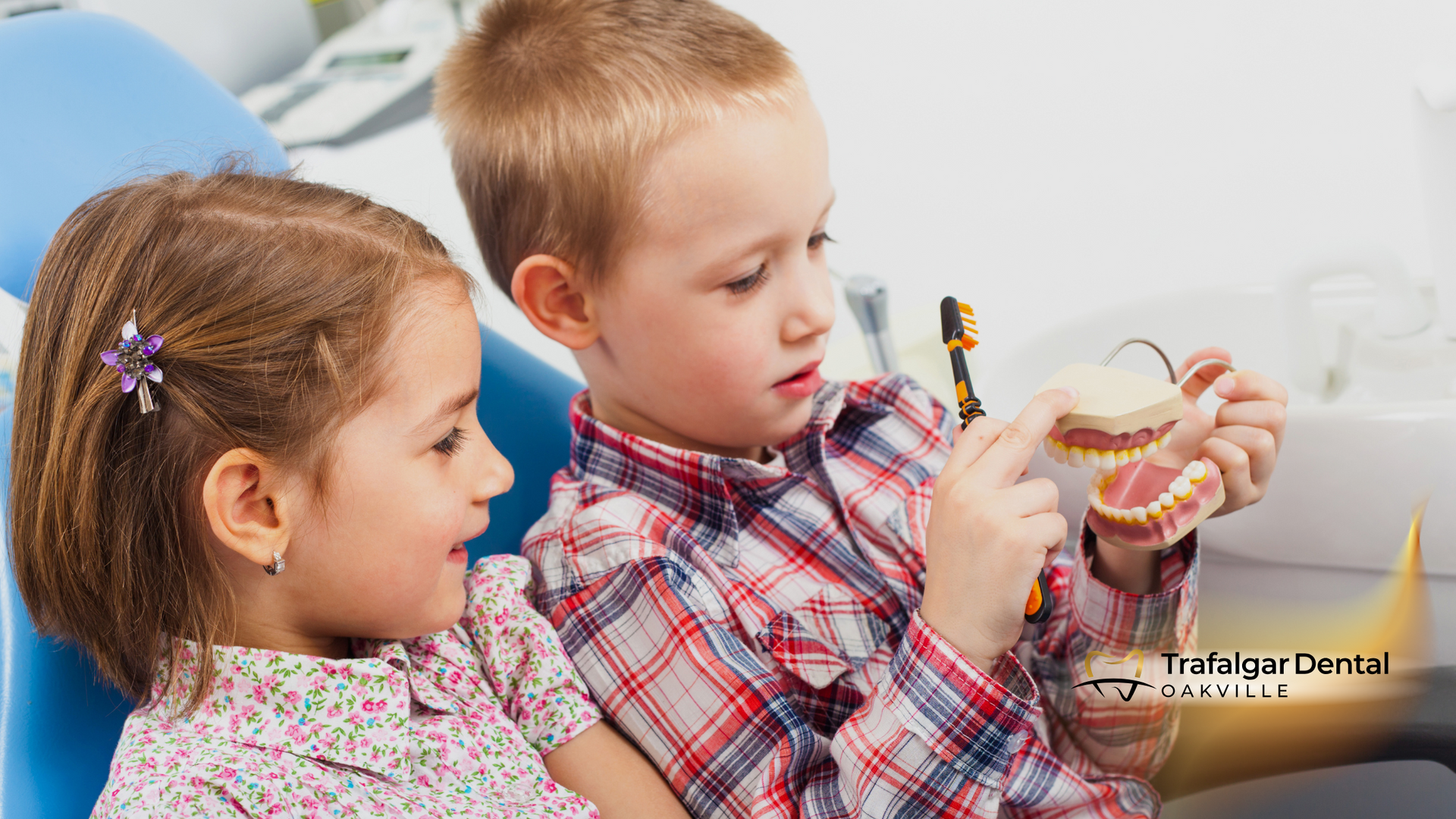 A boy and a girl are sitting in a dental chair looking at a model of teeth.