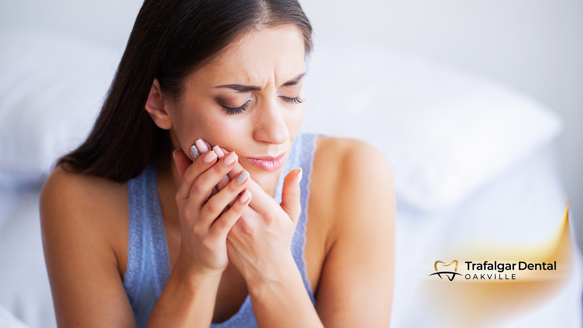 A woman is holding her tooth in pain while sitting on a bed.