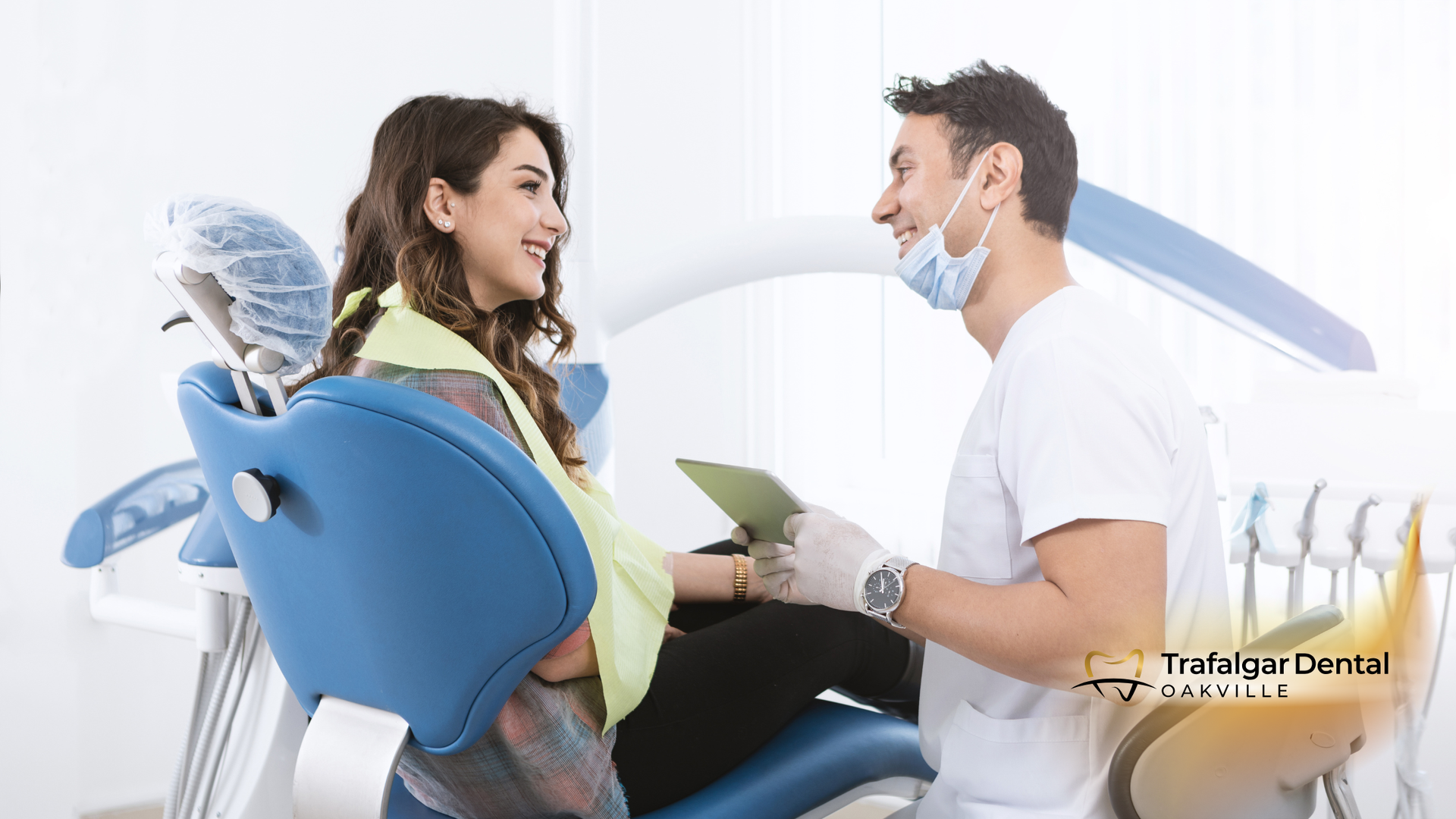 A dentist talking to a patient seated in a dental chair. They are smiling and looking at each other in a bright office.