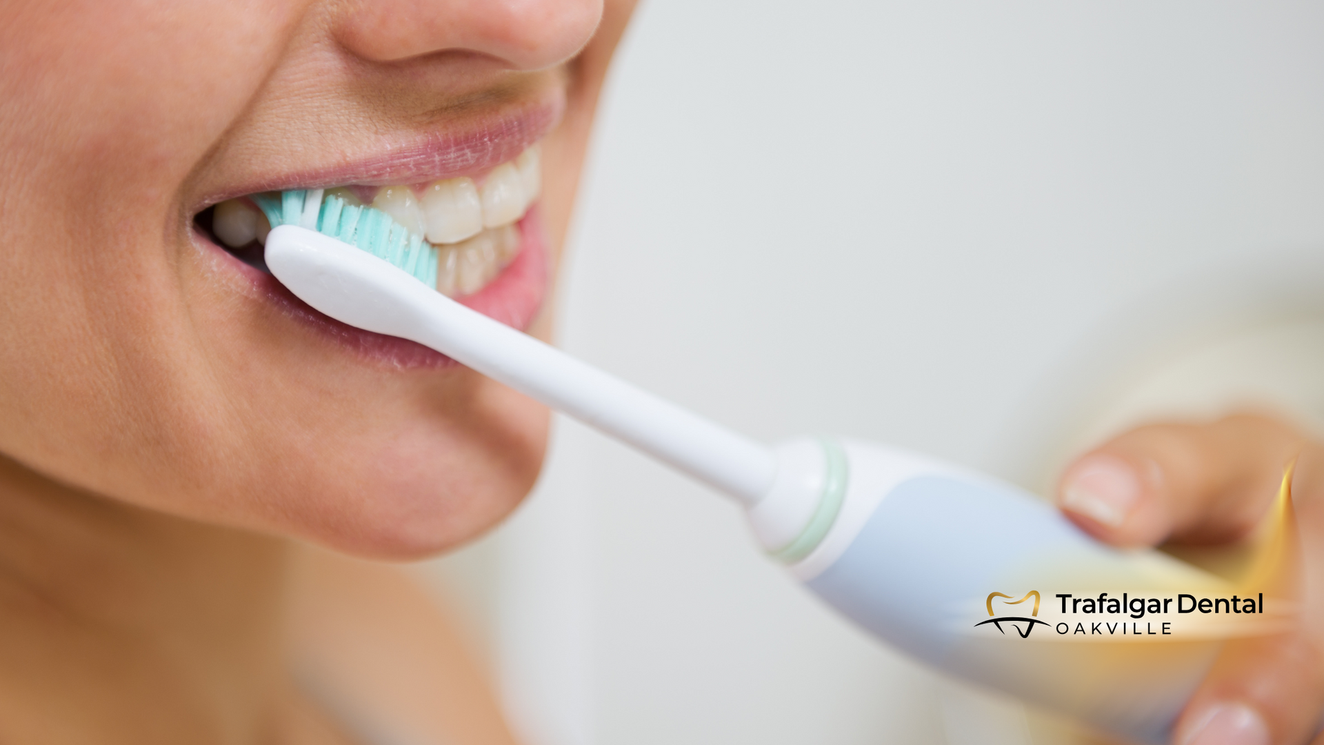 A woman is brushing her teeth with an electric toothbrush.