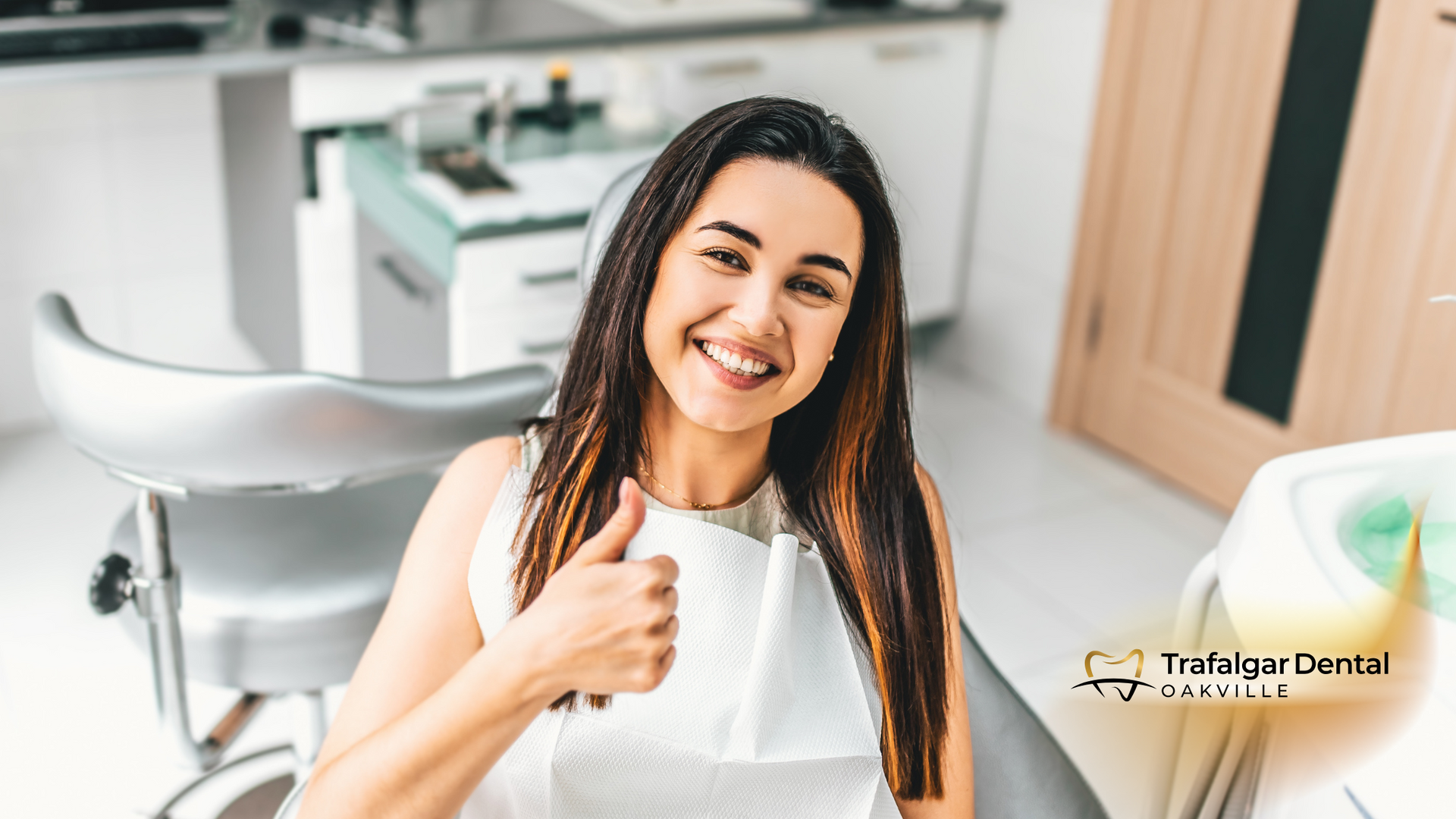 A woman is sitting in a dental chair giving a thumbs up.