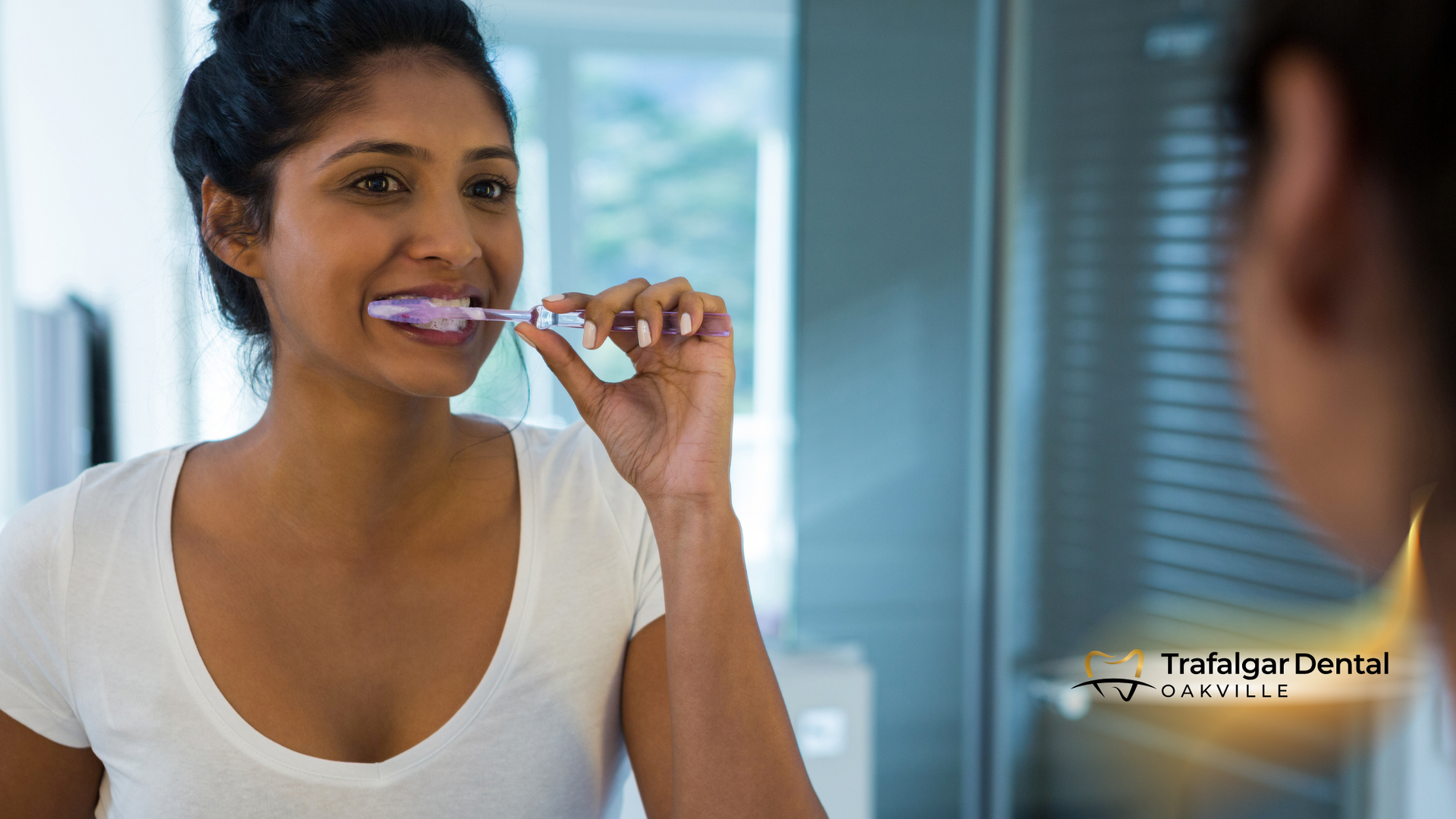 A woman is brushing her teeth in front of a mirror.