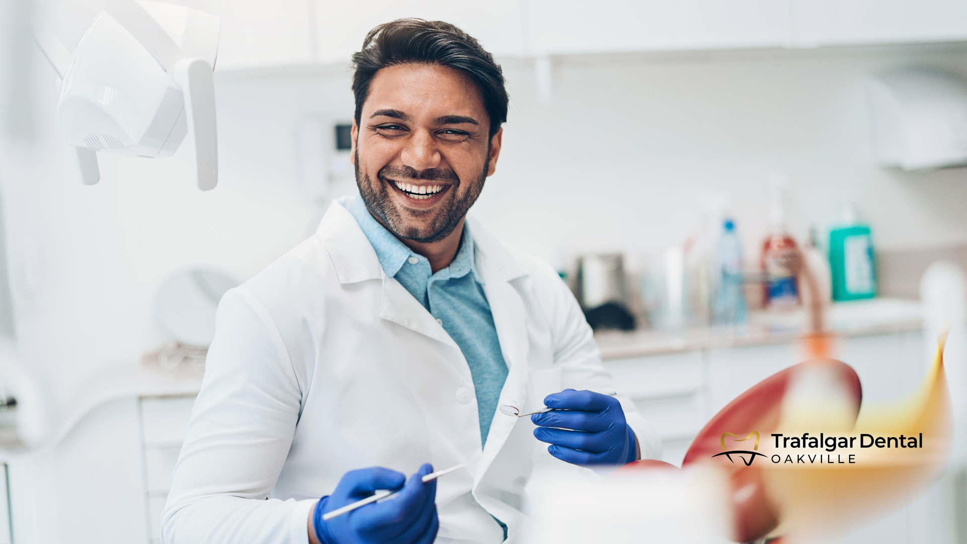 A dentist is smiling while holding a syringe in a dental office.