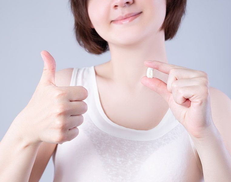 A woman is holding a pill in her hand and giving a thumbs up.