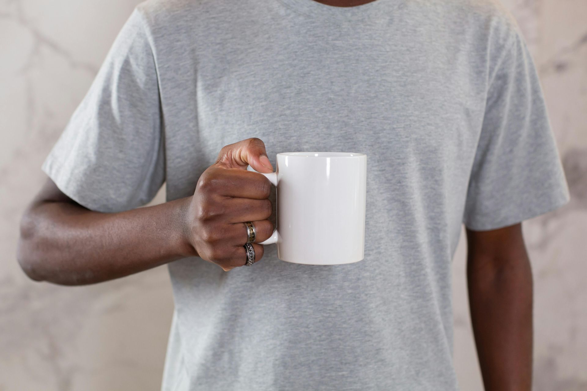 A man in a grey t-shirt is holding a white coffee mug.