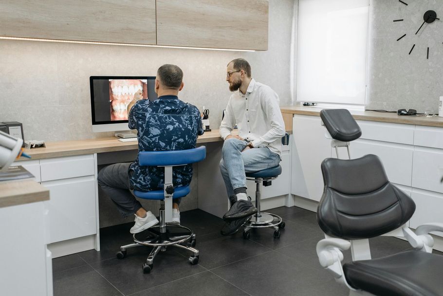 Two men are sitting in a dental office looking at a computer screen.