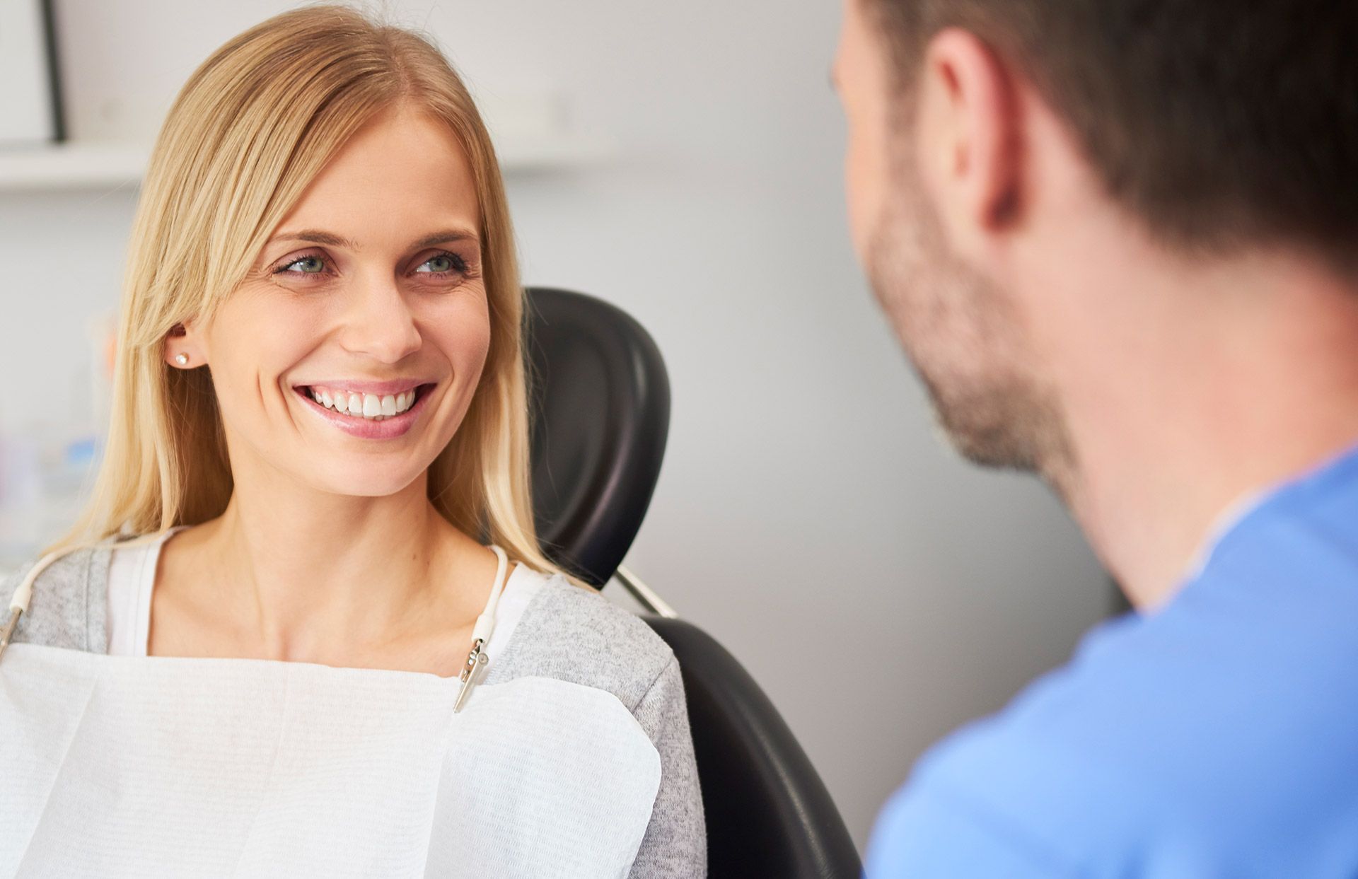 A woman is smiling while sitting in a dental chair talking to a dentist.