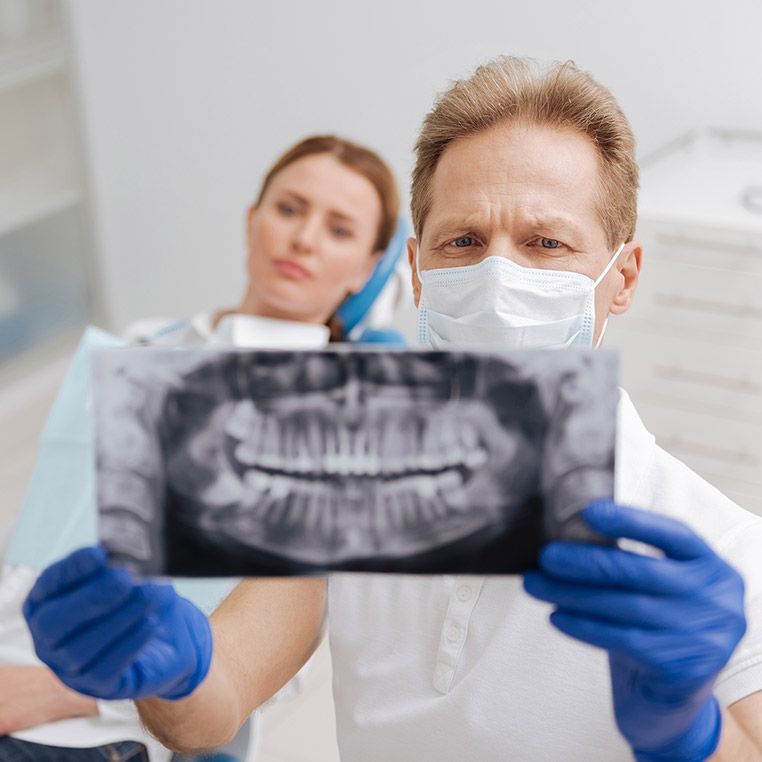 A dentist wearing a mask is holding an x-ray of a patient 's teeth.
