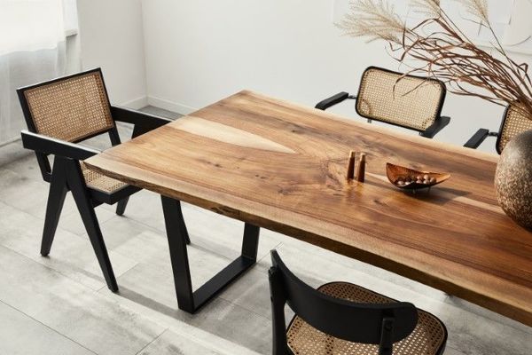 Wooden dining table with black chairs, featuring caned backs and seats, set in a light-filled room.