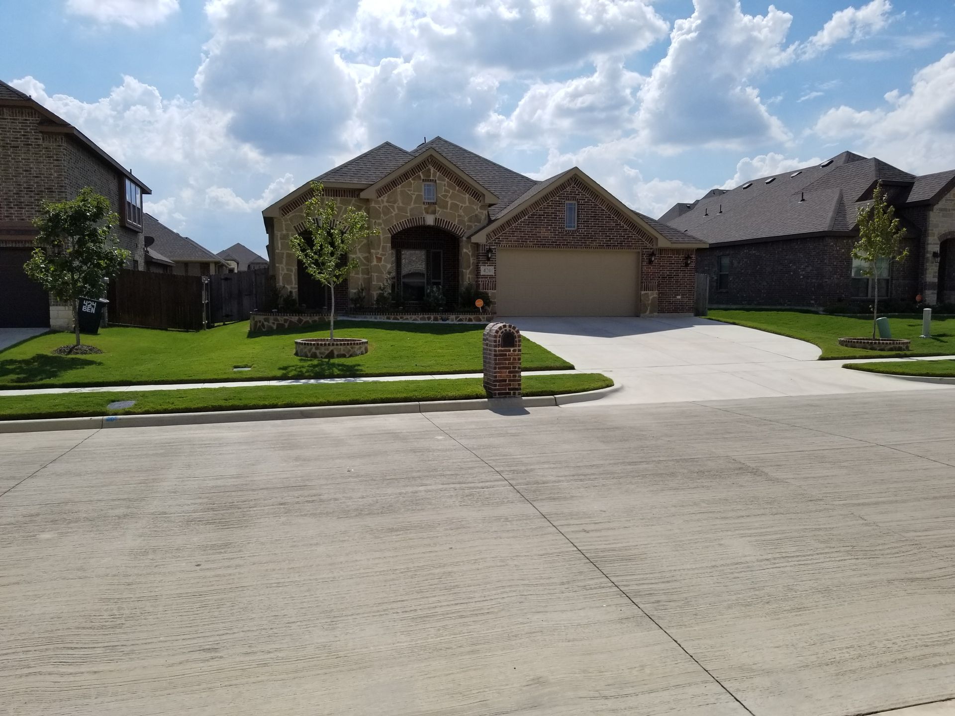 Suburban house with stone facade, two-car garage, and a wide driveway under a blue sky